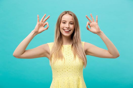 Happy young woman showing ok sign with fingers with big smile isolated on a blue background.