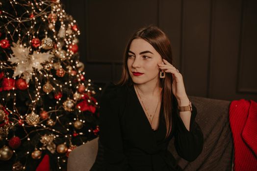 beautiful young woman in a black dress near a Christmas tree in garlands. decorated house for New Year. Christmas morning. apartment interior. Valentine's Day celebration