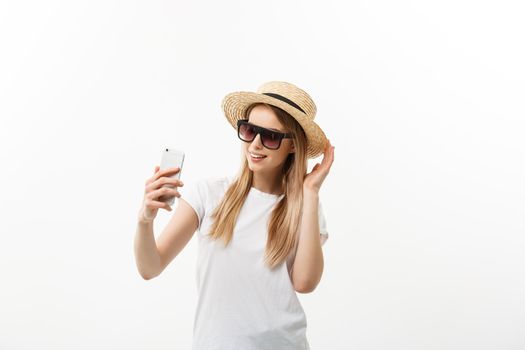 Fashion and Lifestyle Concept: pretty young woman wearing a hat, sunglasses takeing a photo of herself by mobile phone isolated over white background.
