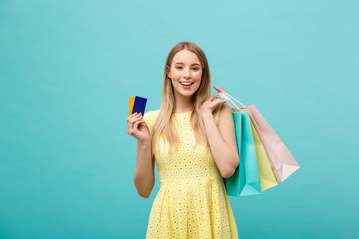 Shopping and Lifestyle Concept: Beautiful young girl with credit card and colorful shopping bags. Isolated on blue background.