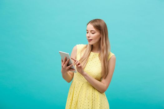 Portrait of a young happy woman holding tablet computer with copy space while standing isolated over blue background.