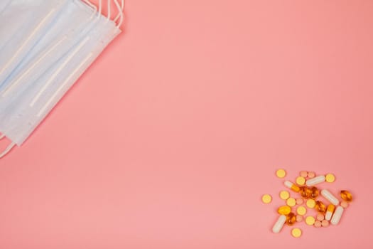 Medical masks with pills of different colors on a pink background. Medical concept with copy space. View from above.