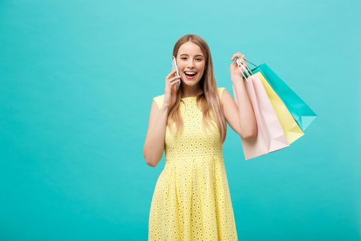 Portrait of happy fashion caucasian woman with shopping bags calling on mobile phone. Isolated on blue background