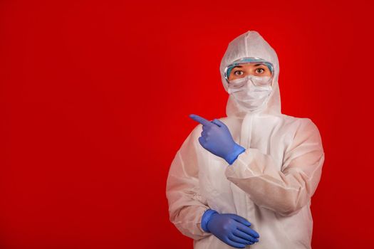 A woman in a protective suit against the COVID-19 virus indicates the direction. Medic woman wearing protective clothing against coronovirus on a red background.