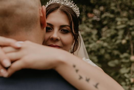 Holovchyntsi, Khmelnytska oblast, Uk raine - 07.12.2020: bride in veil and a tiara on her head hugs the groom and smiles on the woman arm tattoo in the form of flying birds swallows.