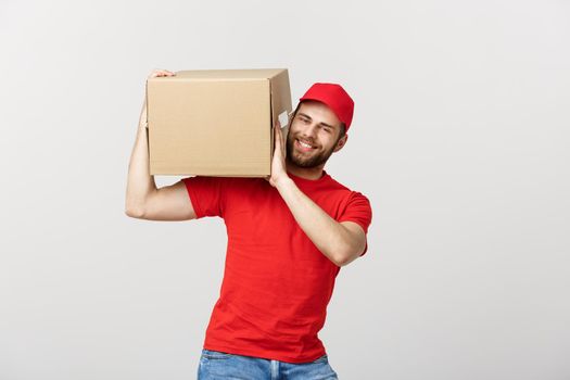 Deliver Concept: Young caucasian handsome delivery man holding a box on shoulder. Isolated over grey background
