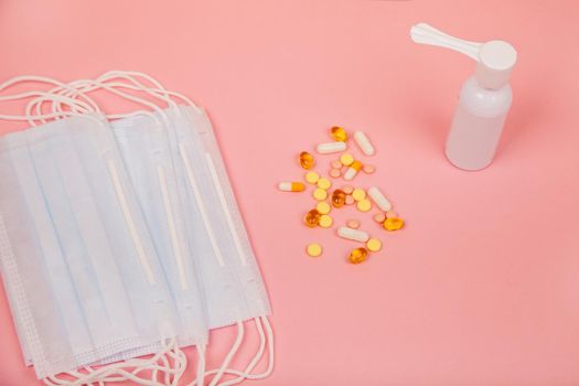 Medical mask, pills and spray for the treatment of throat on a pink background, concept of coronavirus virus and health. Medical concept. View from above.