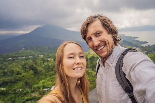 Man and woman making selfie on background of Batur volcano and Agung mountain view at morning from Kintamani, Bali, Indonesia.