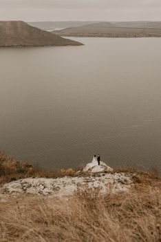 a wedding couple in love, groom and the bride in dress veil stand on Big Stone on cliff and kiss. panoramic view big river lake sea in distance silhouettes of islands. bakota ukraine europe