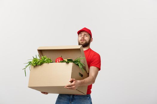 Delivery Concept: Handsome delivery man is holding a heavy grocery box isolated over grey background
