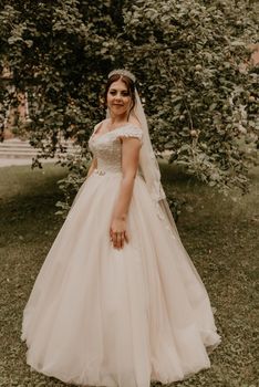 dark-haired European Caucasian young woman bride in white wedding dress with long veil and tiara on head spinning whirls dancing posing moving at nature on background greenery. Valentine love couple