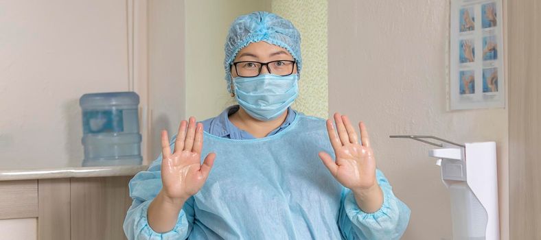 banner with a medical worker in a disposable medical suit, a medical cap and a mask with glasses, shows the treated hands with a disinfectant solution next to the elbow dispenser. soft focus