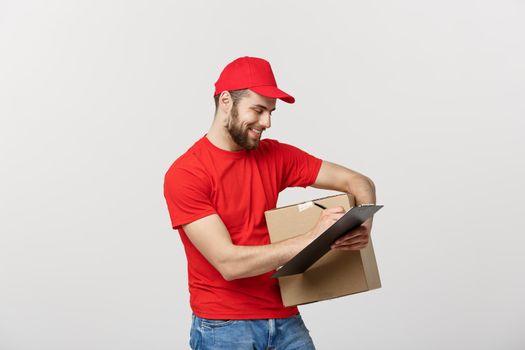 Portrait of smiling male delivery man writing on clipboard and holding box. Isolated over white background.