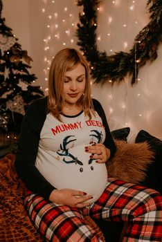 pregnant woman sits in pajamas with on the bed in the bedroom. Christmas morning. New Year's interior. Valentine's Day celebration
