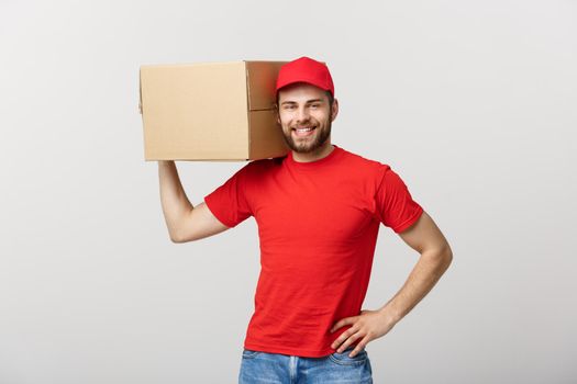 Deliver Concept: Young caucasian handsome delivery man holding a box on shoulder. Isolated over grey background