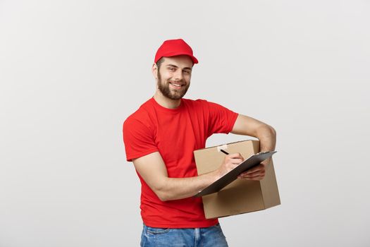 Portrait of smiling male delivery man writing on clipboard and holding box. Isolated over white background.