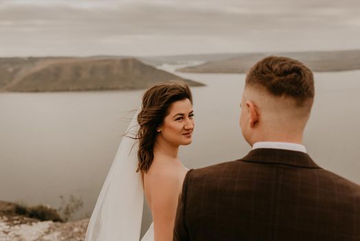 loving couple wedding newlyweds outdoor. bride in white dress long veil and groom in suit walk in summer fall on mountain above river. sunrise. man and woman on rocks above cliff. bakota ukraine