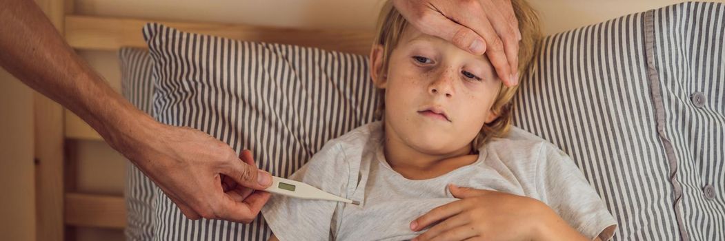 BANNER, LONG FORMAT Sick boy with thermometer laying in bed and father hand taking temperature. father checking temperature of her sick son who has thermometer. Sick child with fever and illness in bed.