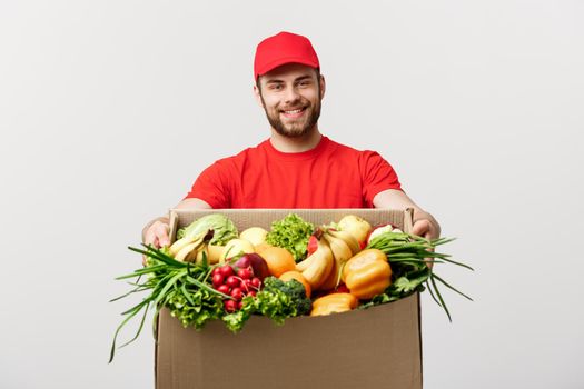 Delivery Concept - Handsome Cacasian delivery man carrying package box of grocery food and drink from store. Isolated on Grey studio Background. Copy Space