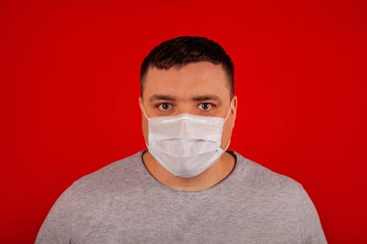 Portrait of a young man looking at the camera in a medical protective mask on a red background.