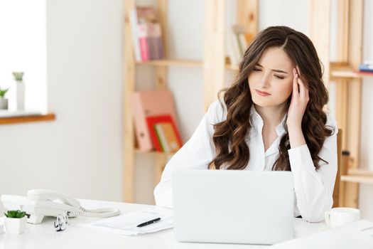 Tired young businesswoman suffering from long time sitting at computer desk in office.