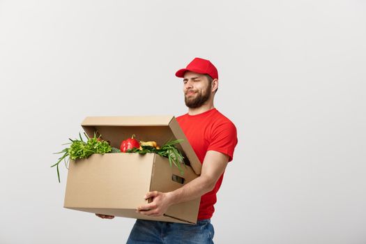 Delivery Concept: Handsome delivery man is holding a heavy grocery box isolated over grey background