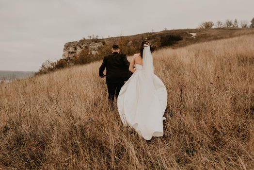 A loving couple wedding newlyweds in a white dress and a suit walk run hug kissing on the tall grass in the summer autumn field on the mountain above the river. sunset. bakota ukraine