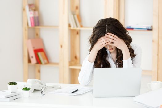 Tired young businesswoman suffering from long time sitting at computer desk in office.