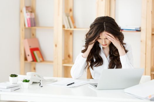 Tired young businesswoman suffering from long time sitting at computer desk in office.