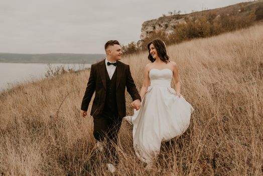 A loving couple wedding newlyweds in a white dress and a suit walk hug kissing on the tall grass in the summer autumn field on the mountain above the river. sunset. bakota ukraine