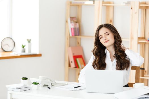 Tired young businesswoman suffering from long time sitting at computer desk in office.