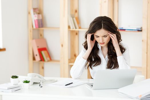 Tired young businesswoman suffering from long time sitting at computer desk in office.