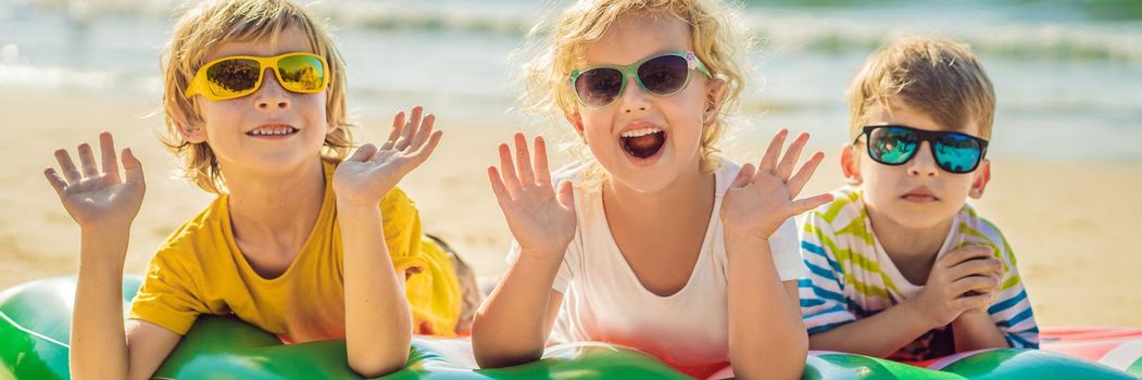 Children sit on an inflatable mattress in sunglasses against the sea and have fun. BANNER, LONG FORMAT