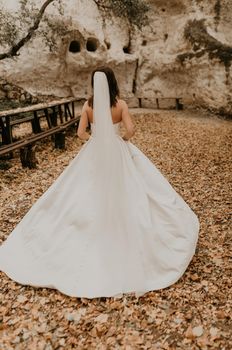 young woman bride in white wedding dress with long veil run away through autumn forest on fallen orange leaves to mountain. brunette with short hair bob