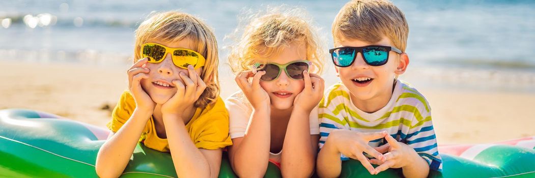 Children sit on an inflatable mattress in sunglasses against the sea and have fun. BANNER, LONG FORMAT