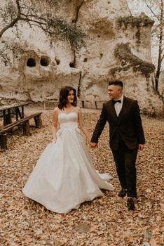 wedding couple in love man and woman walking in autumn forest background of stone rocks. groom suit and bride dress with long veil on short hair outdoors. rock monastery in bakota