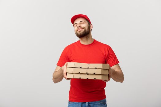 Delivery Concept: Handsome Pizza delivery man showing delicious expression over grey background.