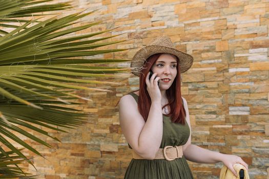 young red-haired girl, calling the hotel reception on her summer holiday. travel and leisure. tourist in a tropical resort. outside, natural sunlight,