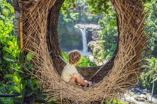 Bali trend, straw nests everywhere. Child friendly place. Boy tourist enjoying his travel around Bali island, Indonesia. Making a stop on a beautiful hill. Photo in a straw nest, natural environment. Lifestyle. Traveling with kids concept. What to do with children.