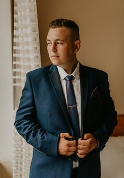 blonde European Caucasian young groom in shirt business suit with tie prepare for wedding. a man preparing for an important event a meeting indoors worries