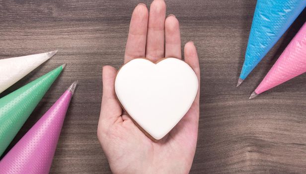 Hand holding white heart shape cookie for Mothers day, Womans day or Valentines Day on wooden background. Copy space.