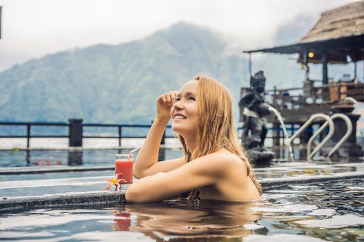 Geothermal spa. Woman relaxing in hot spring pool against the lake. hot springs concept. Drinking guava juice.