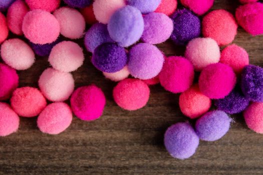 Round pink and purple fluffy balls pompoms on wooden background. Bunch of poppoms