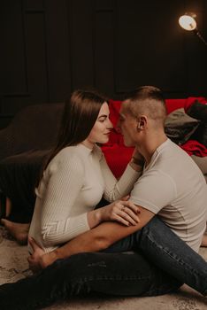 in love couple man and woman sitting on floor cross-legged embrace hugging and kiss Christmas tree. decorated house for New Year. Christmas morning. apartment interior. Valentine's Day celebration