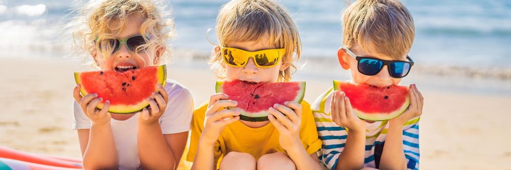 Children eat watermelon on the beach in sunglasses. BANNER, LONG FORMAT