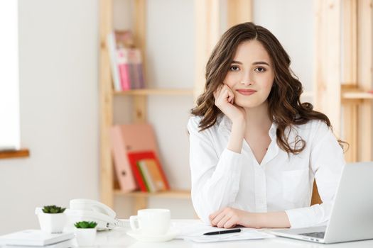 Young attractive woman at a modern office desk, working with laptop and thinking about something
