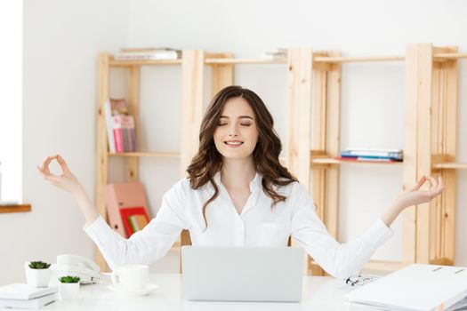 Business and Health Concept: Portrait young woman near the laptop, practicing meditation at the office desk, in front of laptop, online yoga classes, taking a break time for a minute