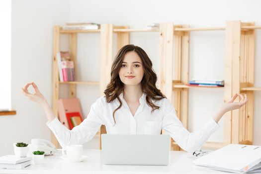 Business and Health Concept: Portrait young woman near the laptop, practicing meditation at the office desk, in front of laptop, online yoga classes, taking a break time for a minute