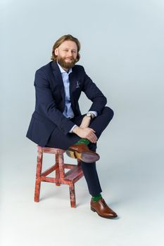 a handsome brutal bearded and long-haired man, a stylish businessman sitting on a chair with a white background. High quality photo