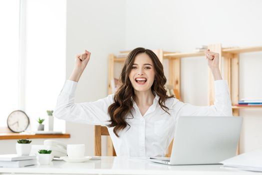 Successful business woman with arms up sitting in modern office